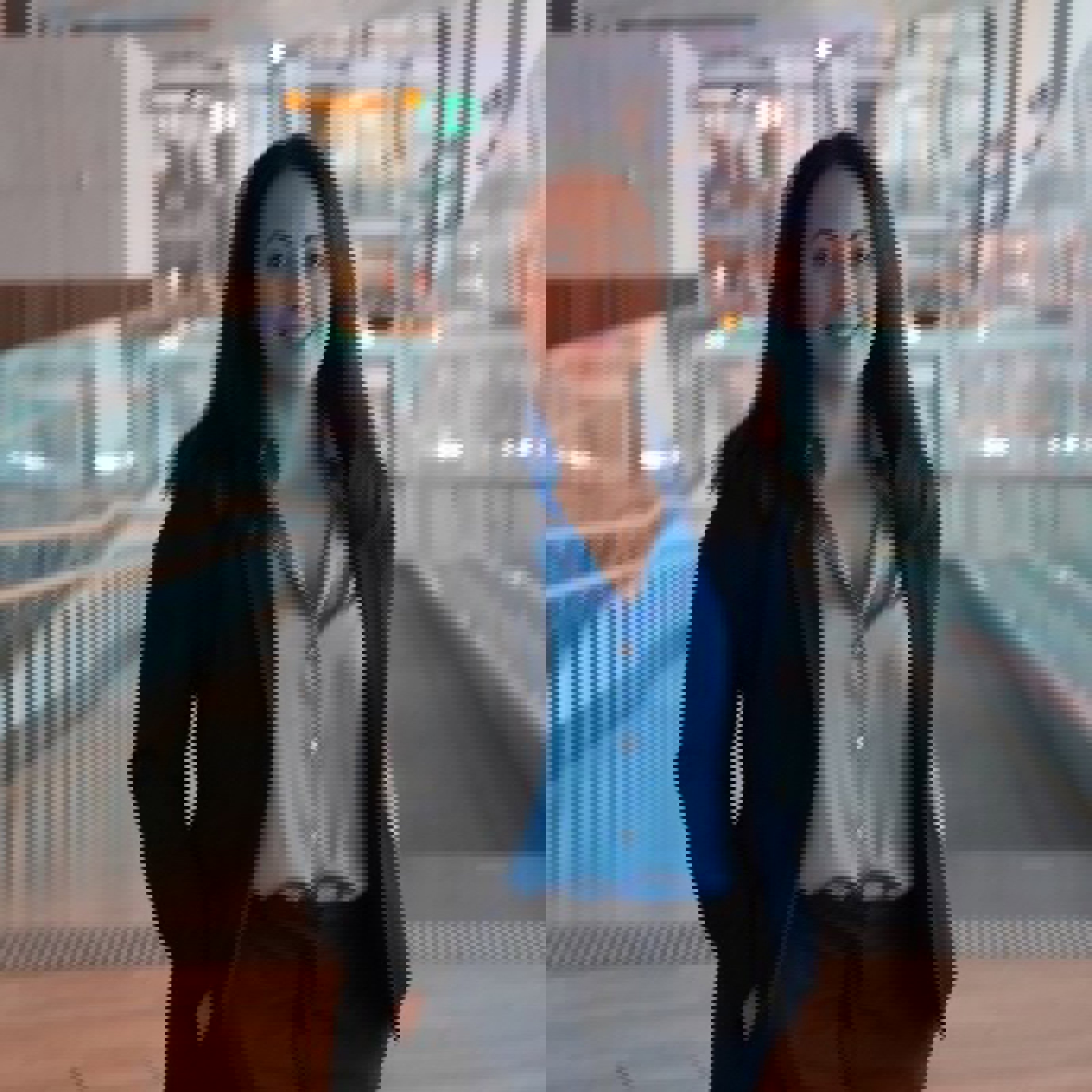 Kvinne i blå skjorte og mørk blazer står i en moderne bygning med glassvegger.