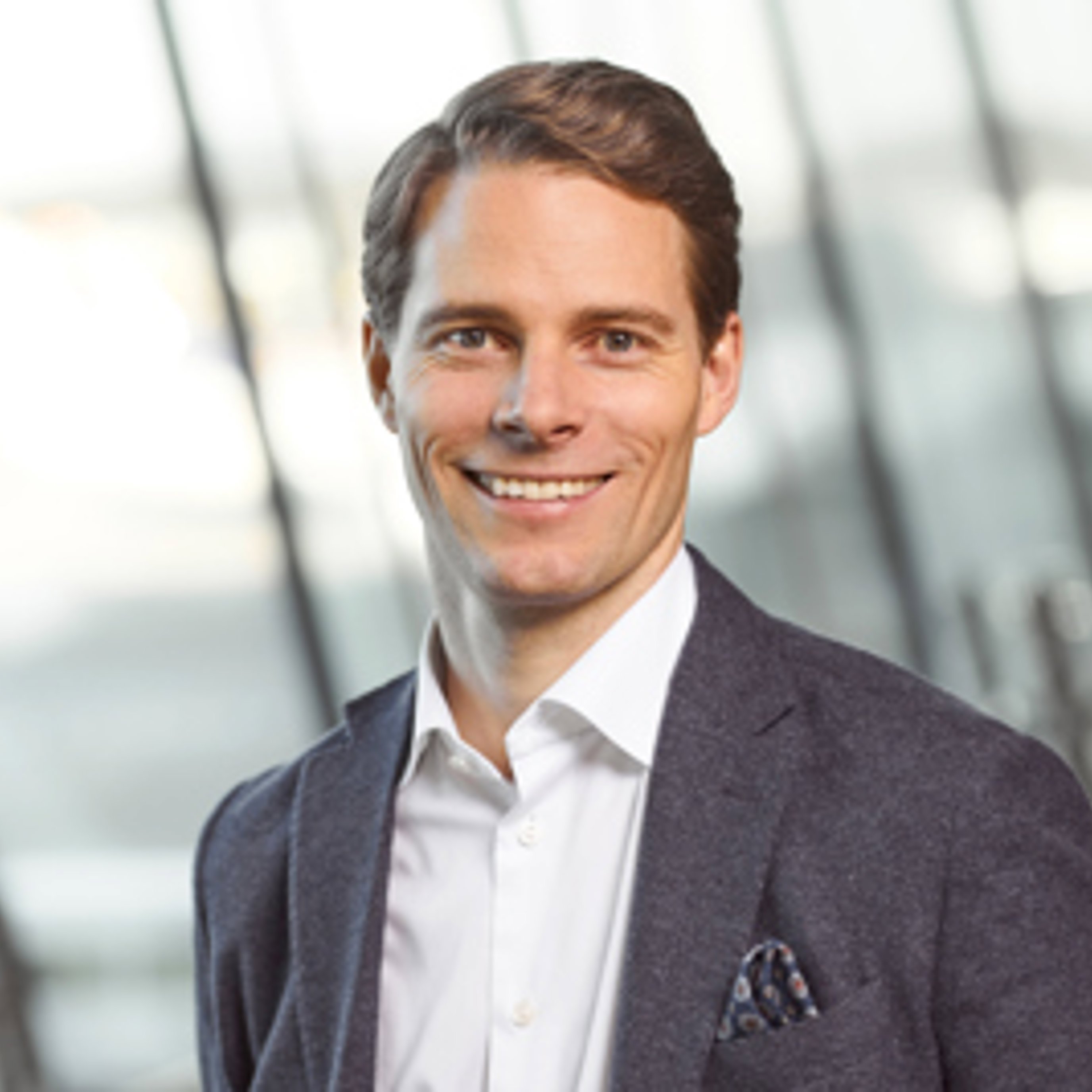 Smilende mann i dress med en uskarp moderne kontorbakgrunn