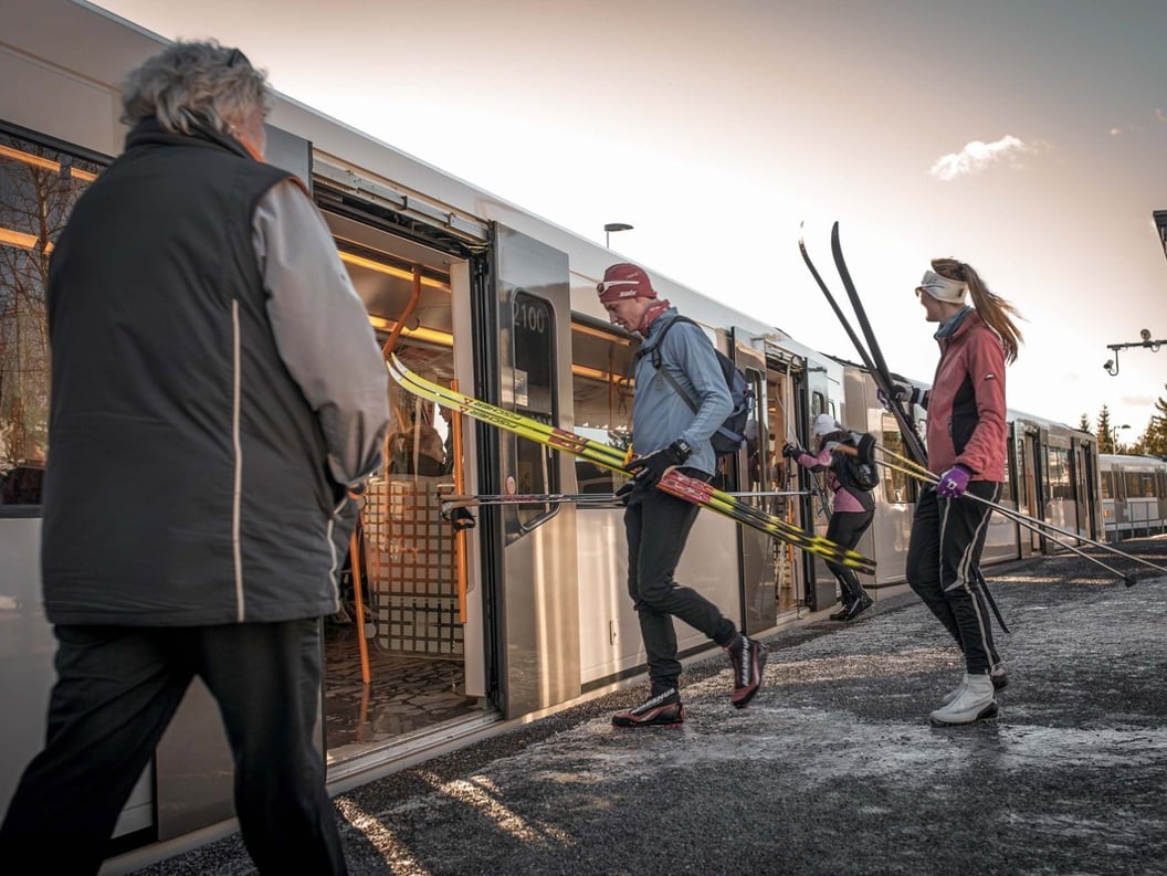 Personer med ski går ombord på en T-banevogn en vinterdag, klare for en skitur.